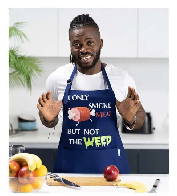Man wearing a blue apron with humorous text in a kitchen setting