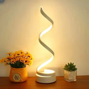 Spiral LED lamp on a wooden surface with decorative plants