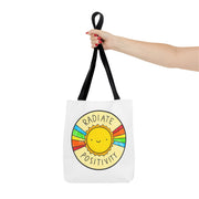 Tote bag with a sun design and 'Radiate Positivity' text, held by a hand on a white background