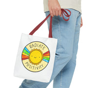 Tote bag with a sun design and 'Radiate Positivity' text held by a person wearing jeans.
