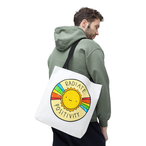 Person wearing a green hoodie with a white tote bag featuring a sun design and 'Radiate Positivity' text.