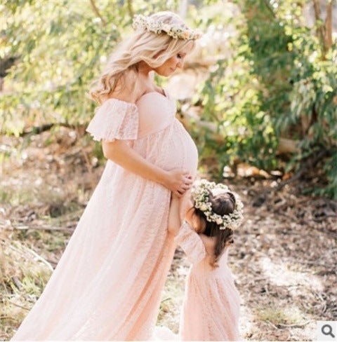 Pregnant woman and child in matching dresses with floral crowns outdoors.