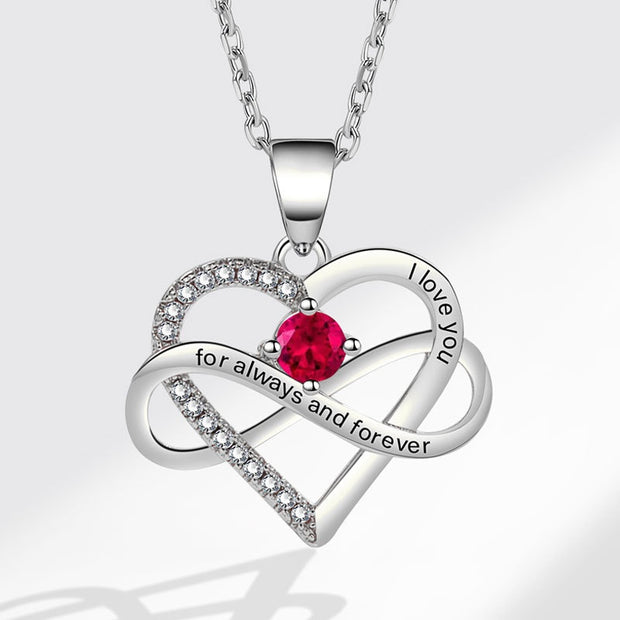 Heart-shaped silver necklace with a red gemstone and engraved text on a white background