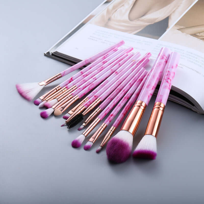 Set of makeup brushes with pink and rose gold handles on a light gray surface.