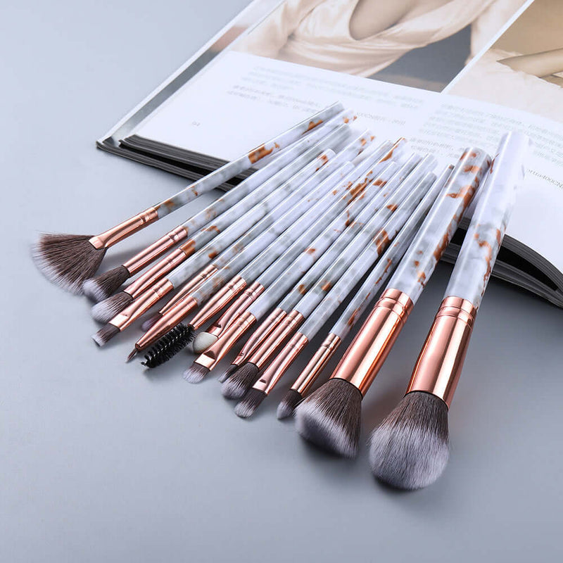 Set of makeup brushes with rose gold handles on a light gray surface.