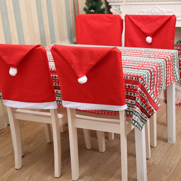 Dining table set with red Santa hat chair covers and a patterned tablecloth.