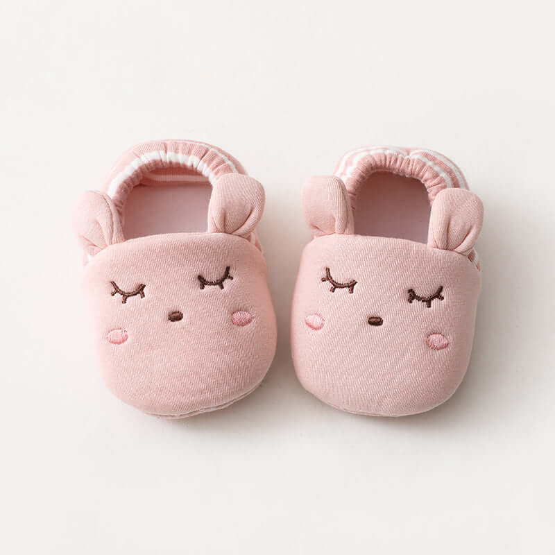 Pair of pink baby slippers with face designs on a white background