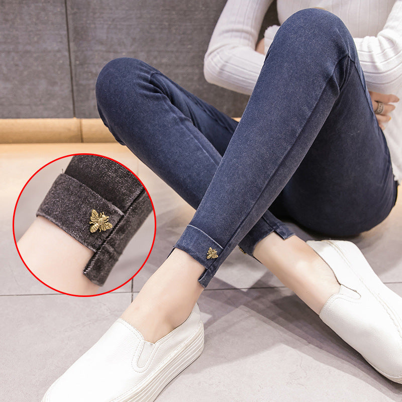 Person wearing blue jeans with a close-up of a rolled-up cuff showing a gold bee design.