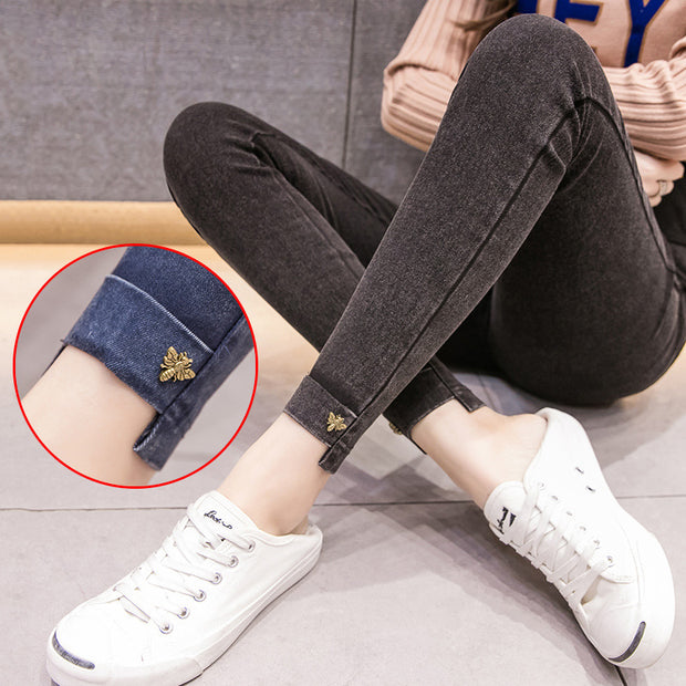 Person wearing dark jeans with rolled-up cuffs and white sneakers sitting on a couch.