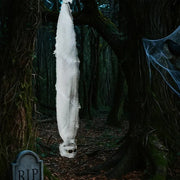 Ghostly figure wrapped in white sheet hanging from a tree in a dark forest with tombstone.