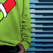 Person wearing a green sweater with a red and white design, standing against a blue and gray striped background.