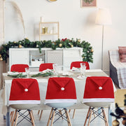 Dining table set with Santa hats on chairs, decorated room in the background