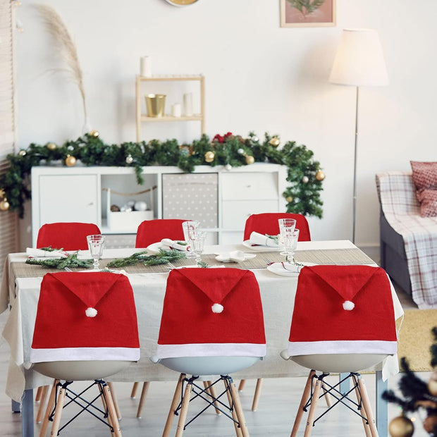Dining table set with Santa hats on chairs, decorated room in the background