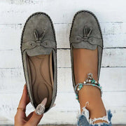 Gray loafers with decorative bow and anklets on a white wooden floor.