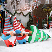 Inflatable Christmas gnomes and tree in a snowy outdoor setting with holiday decorations.