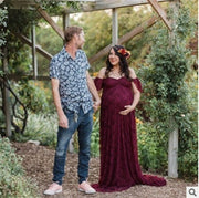 Man and woman holding hands in a garden setting, woman wearing a burgundy maternity dress.
