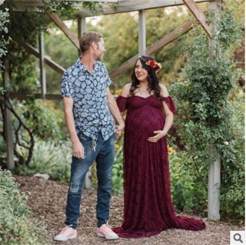 Man and woman holding hands in a garden setting, woman wearing a burgundy maternity dress.