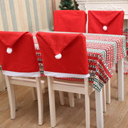Dining table set with red Santa hat chair covers and a patterned tablecloth.