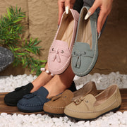 Pair of pink loafers held above a collection of various colored loafers on pebbles.