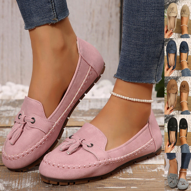 Pink loafers worn with denim jeans on a wooden floor.