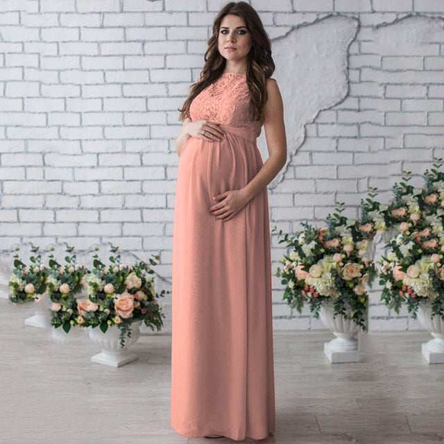 Woman in a long pink dress standing in front of a white brick wall with floral arrangements.