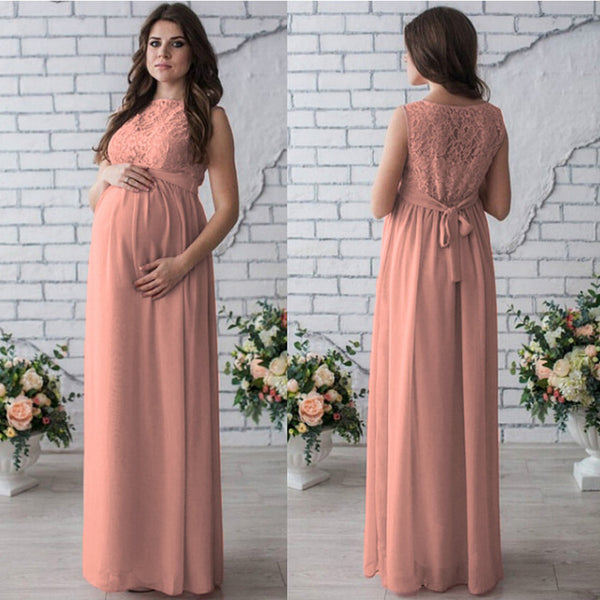 Peach-colored lace dress worn by a model against a white brick wall with floral decorations.