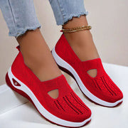 Red slip-on shoes with cut-out design worn by a person on a light background