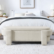 Beige storage bench in front of a bed with white bedding in a bedroom setting.