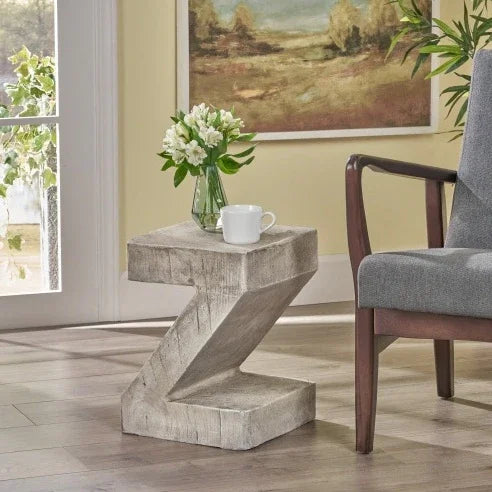 Z-shaped side table with a cup and flowers in a room with a painting on the wall.