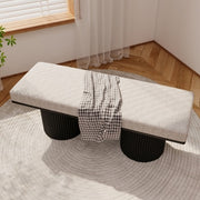 Gray cushioned bench with black cylindrical legs in a room with wooden flooring and a window.