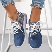 Blue patterned sneakers worn with light blue jeans resting on a chair with white background
