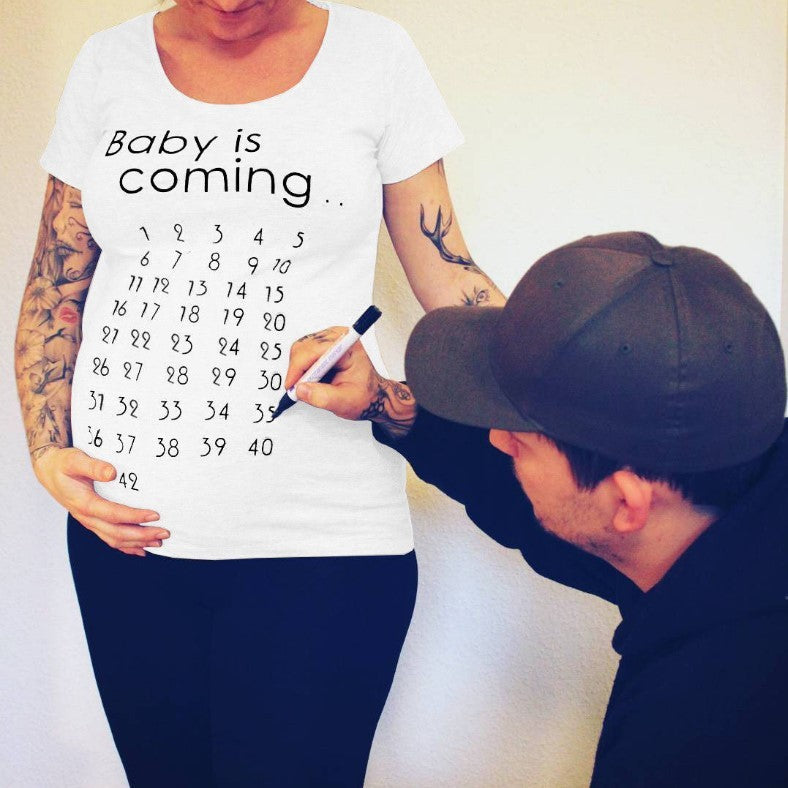 Person wearing a white t-shirt with a countdown pregnancy message, being measured by a man.