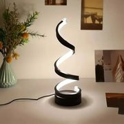 Modern spiral table lamp on a surface with a vase of flowers in the background