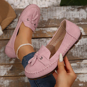 Pink loafers with tassels held by a hand on a wooden surface
