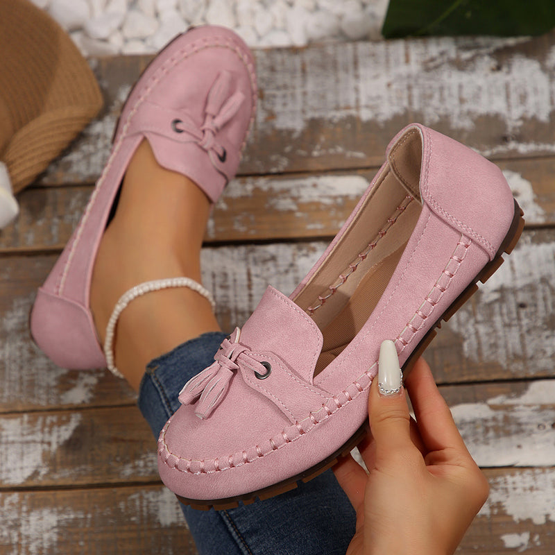 Pink loafers with tassels held by a hand on a wooden surface