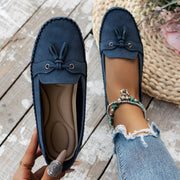 Blue loafers with tassels worn by a person on a wooden floor.