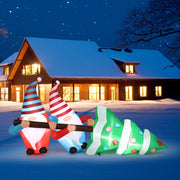 Inflatable Christmas gnomes and tree in front of a snow-covered house at night.