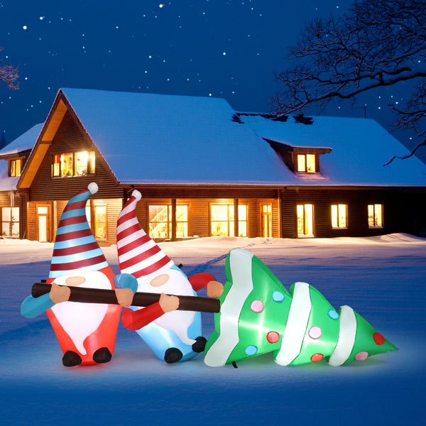 Inflatable Christmas gnomes and tree in front of a snow-covered house at night.