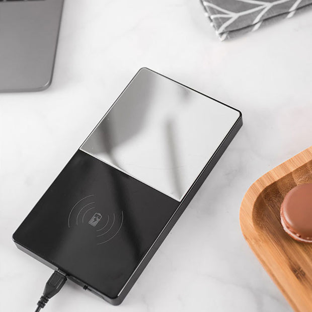 Wireless charging pad on a white surface with a wooden coaster and macaron in the background