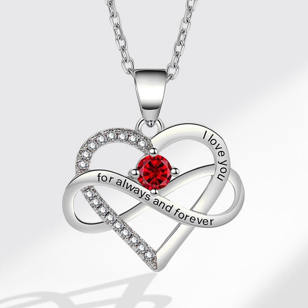 Heart-shaped silver necklace with a red gemstone and engraved text on a white background