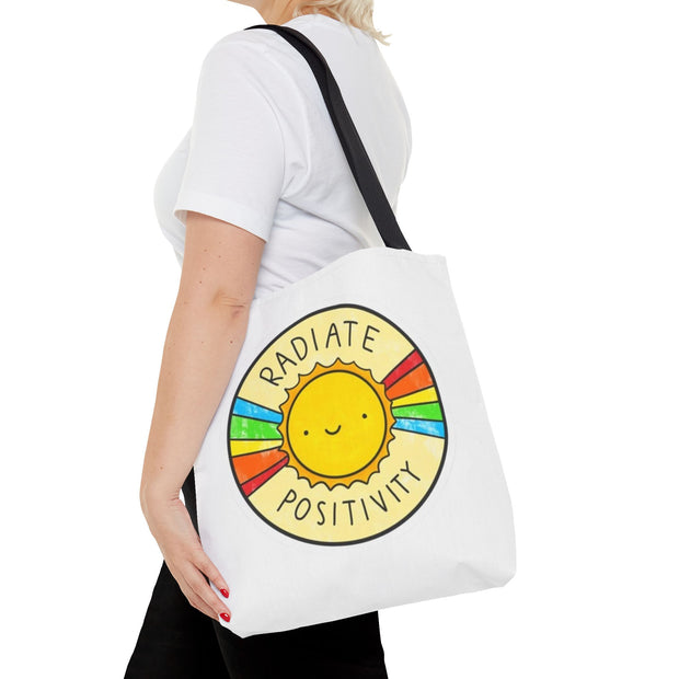 Person holding a tote bag with a sun design and 'Radiate Positivity' text on a white background