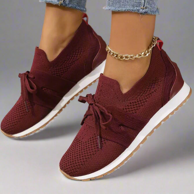 Maroon sneakers worn with jeans on a grey back ground.