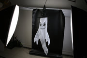 Halloween-themed ghost decoration with a black hat on a black background, illuminated by studio lights.