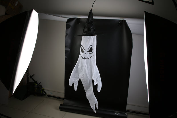 Halloween-themed ghost decoration with a black hat on a black background, illuminated by studio lights.