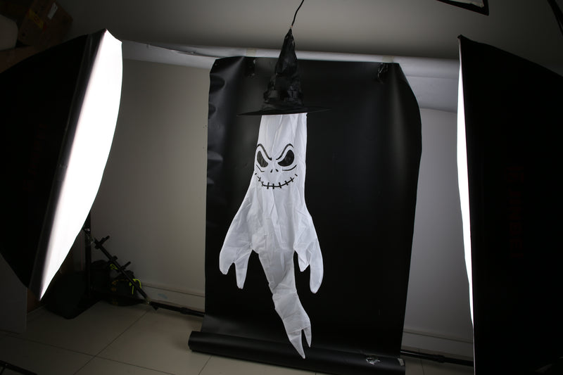 Halloween-themed ghost decoration with a black hat on a black background, illuminated by studio lights.