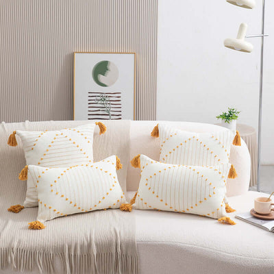 White pillows with gold tassels on a beige sofa in a living room setting.