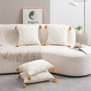 White pillows with gold tassels on a beige sofa in a living room setting.