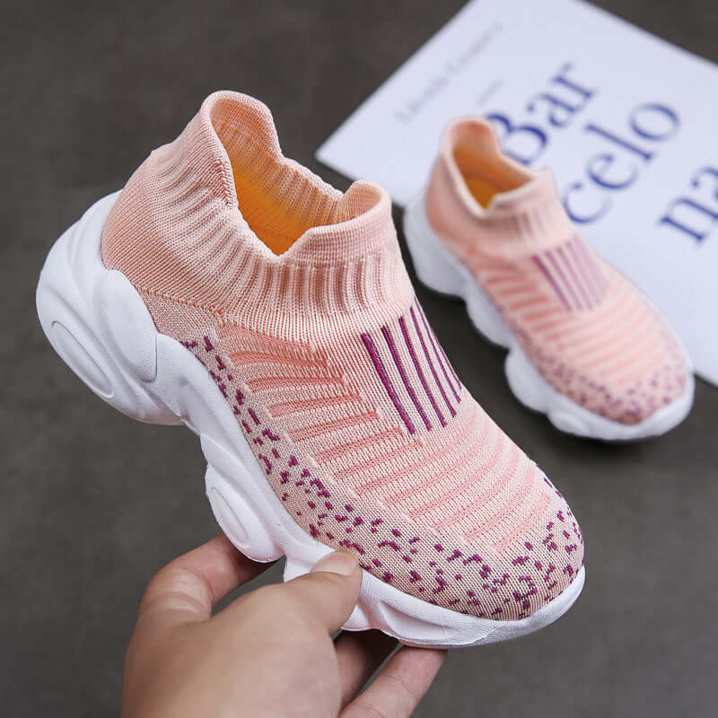 Pink and white children's sock shoes held by a hand on a dark surface.