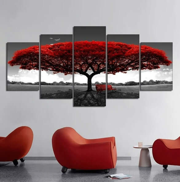 Five-panel wall art of a red tree with a bench, placed above modern red chairs in a room.