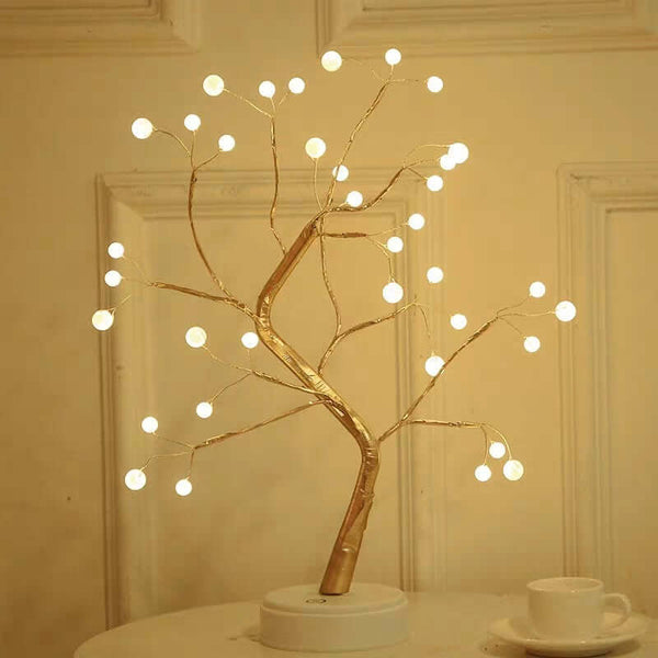 Decorative LED tree with lights on a white surface against a beige wall.
